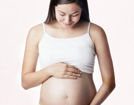 Schwangere Frau halt ihren Bauch vor rosa Hintergrund