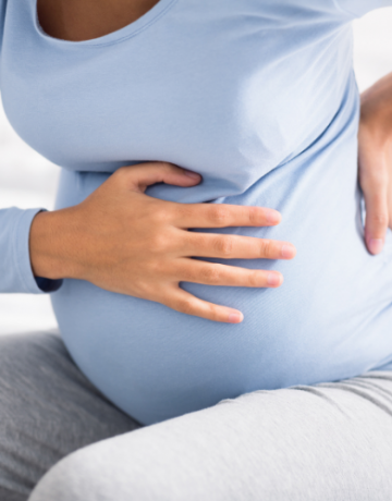 Frau mit Babybauch fasst sich an den Rücken